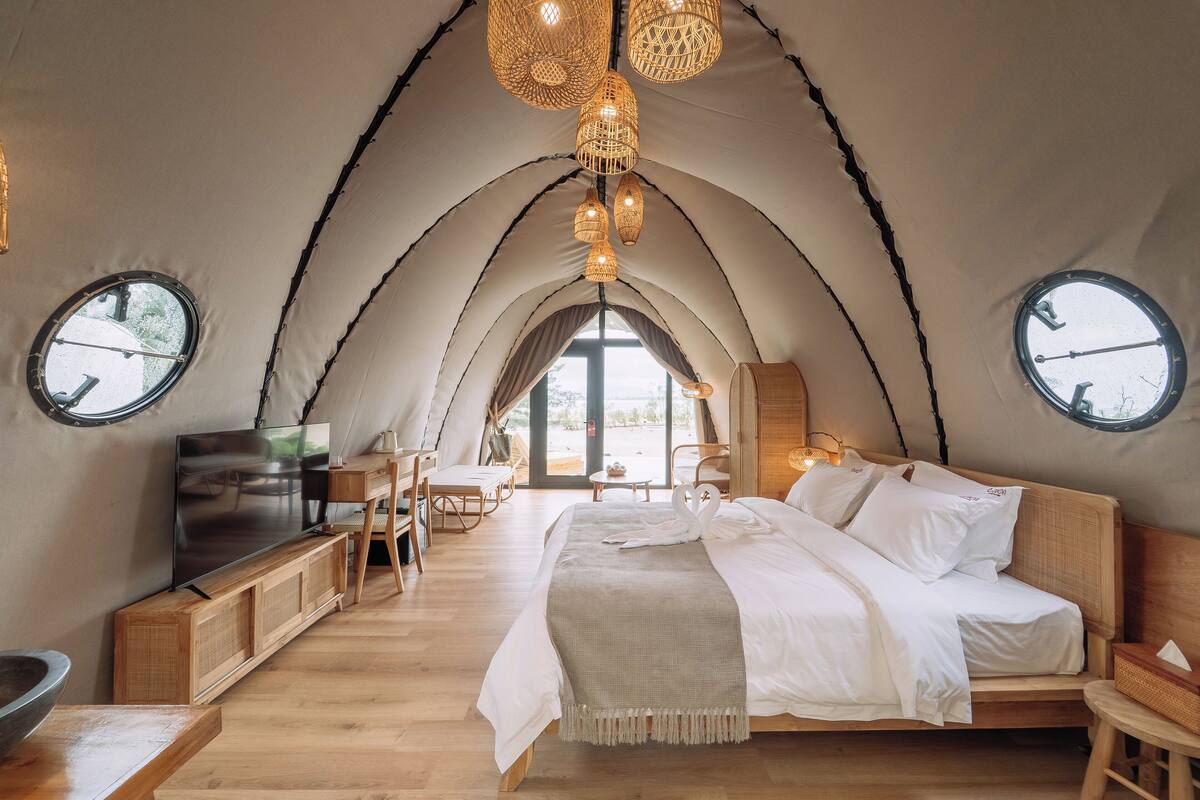 A cozy tented accommodation with a large bed, wooden furniture, and a TV.