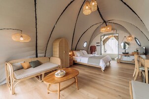 A cozy, well-lit tent-style room with a sofa, a wooden table, a bed, and a dining area.