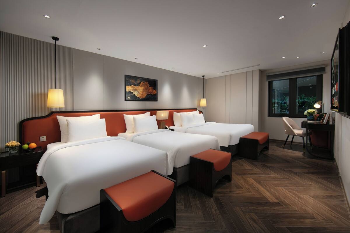 A hotel room with two beds, a desk, a chair, and a window with a view.