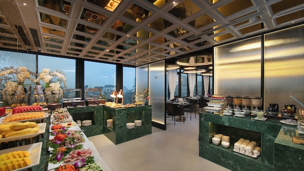 A buffet area with various food items and a view of the cityscape through large windows. - Le Premier Hotel & Rooftop Bar (Hanoi)