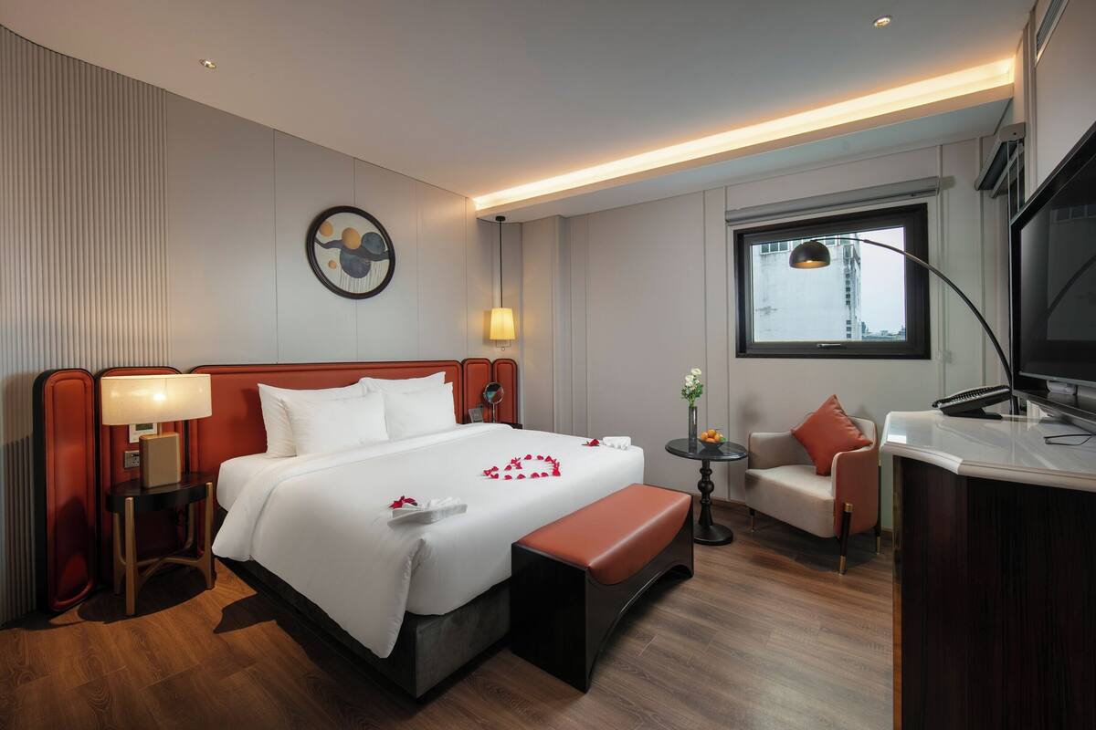 A hotel room with a large bed, a desk, a chair, a TV, and a window.