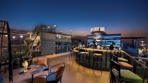 A rooftop bar with a bar counter, stools, and a view of the cityscape at dusk. - Le Premier Hotel & Rooftop Bar (Hanoi)