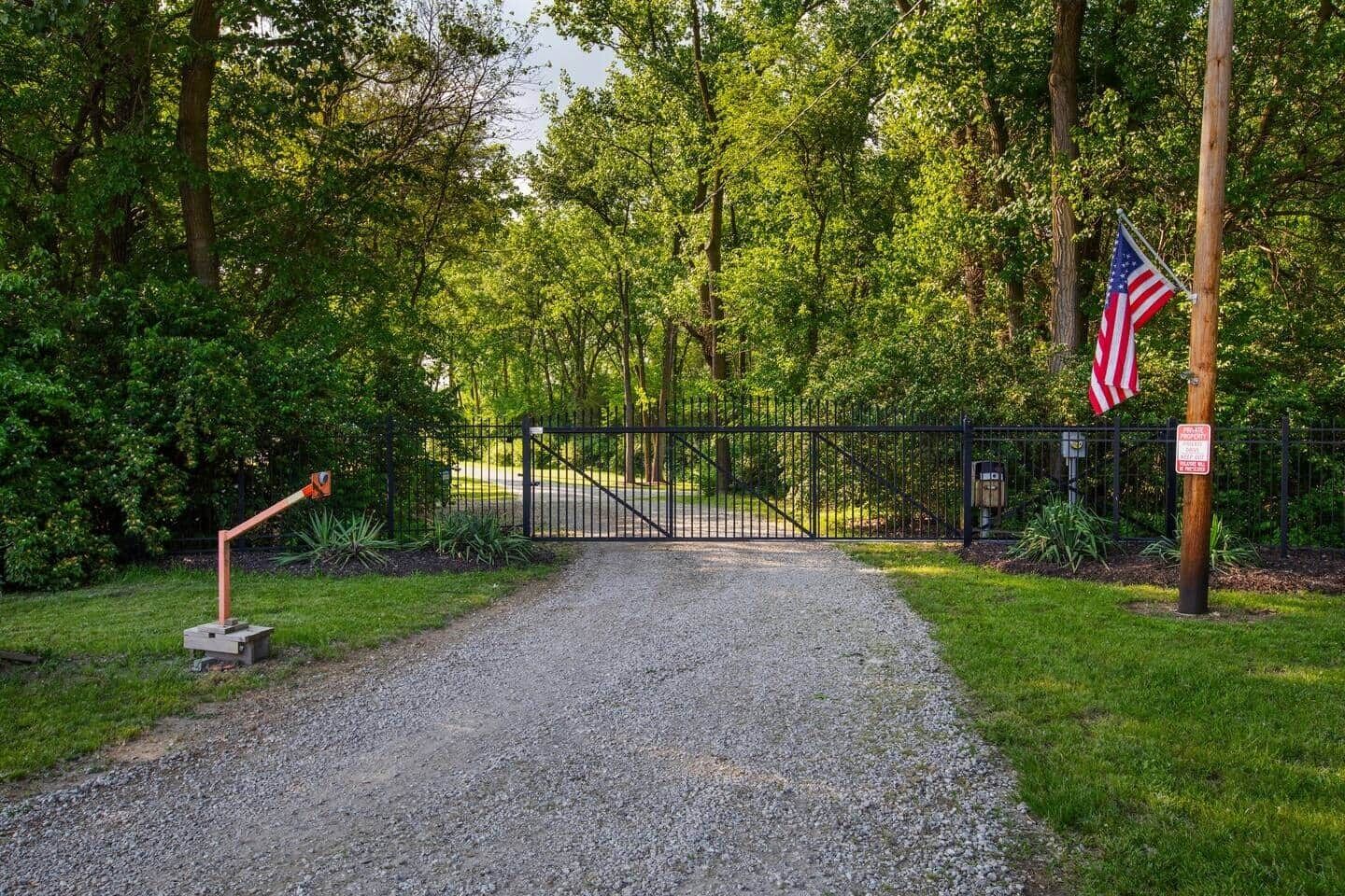 A gravel path leading to a gated entrance with an American flag, surrounded by lush greenery.