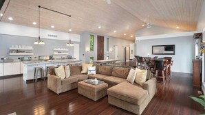 Un vaste espace de vie comprenant un grand canapé d’angle, une table à manger avec des chaises, une cuisine équipée d’appareils électroménagers modernes et un ventilateur de plafond.