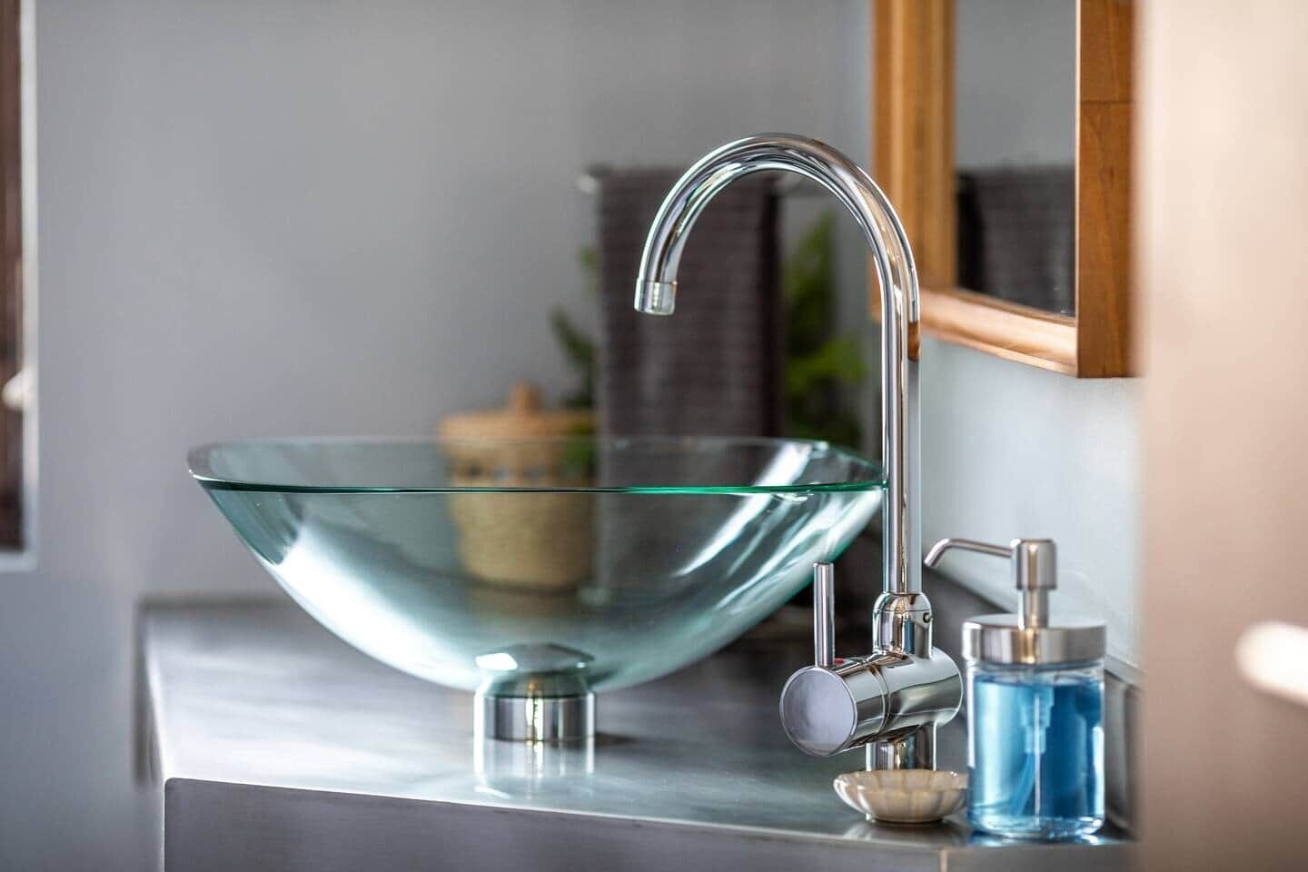 Ein modernes Badezimmer mit einem Waschbecken aus Glas, einem chromfarbenen Wasserhahn und einem Spiegel.
