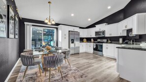 A modern kitchen with white cabinetry, stainless steel appliances, and a glass dining table. - Modern home near rainbow river Springs to enjoy with family and friends  (Dunnellon)