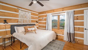 A wooden-paneled room with a bed, a small table, a lamp, and a window with curtains. - Boone/Blowing Rock Cabin: Hot Tub, Mountain Views, Sleeps 8, Peaceful, Private (Vilas)