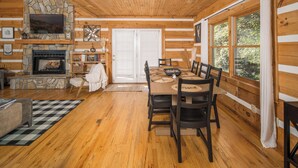 A cozy cabin interior with a stone fireplace, wooden dining table, and large windows. - Boone/Blowing Rock Cabin: Hot Tub, Mountain Views, Sleeps 8, Peaceful, Private (Vilas)
