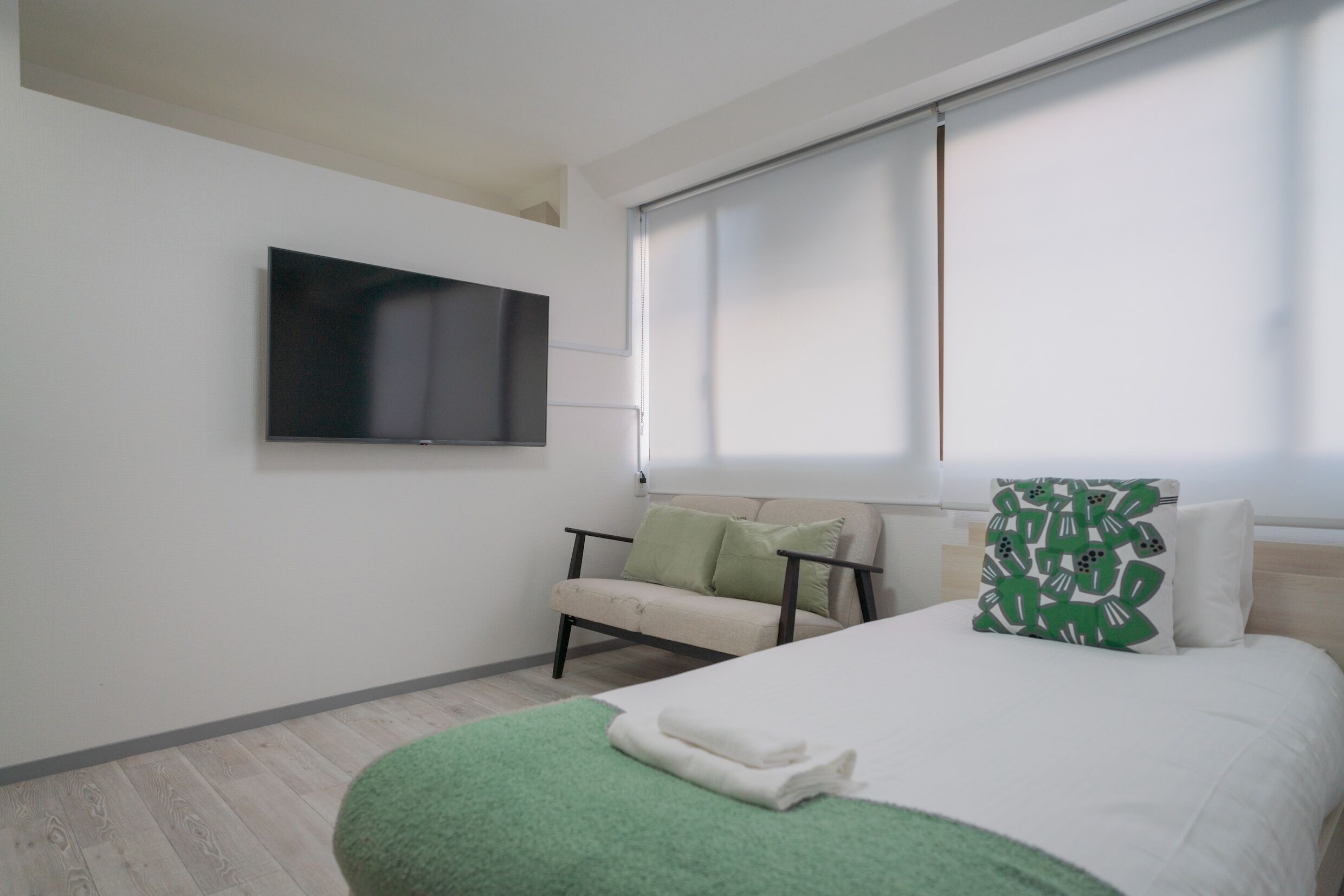 Une chambre d’hôtel moderne, équipée d’un lit, d’un canapé, d’un téléviseur fixé au mur et d’une fenêtre avec des stores.