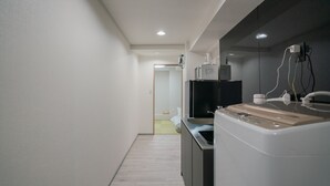 A modern kitchen with a built-in microwave, coffee maker, and a large appliance, likely a washer and dryer, in a hallway with a wooden floor and a door leading to another room. - STAY OSAKA NANBA (Osaka)