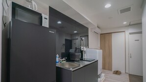 A modern kitchen with a black refrigerator, a sink, and a microwave. There is a wooden door in the background. - STAY OSAKA NANBA (Osaka)
