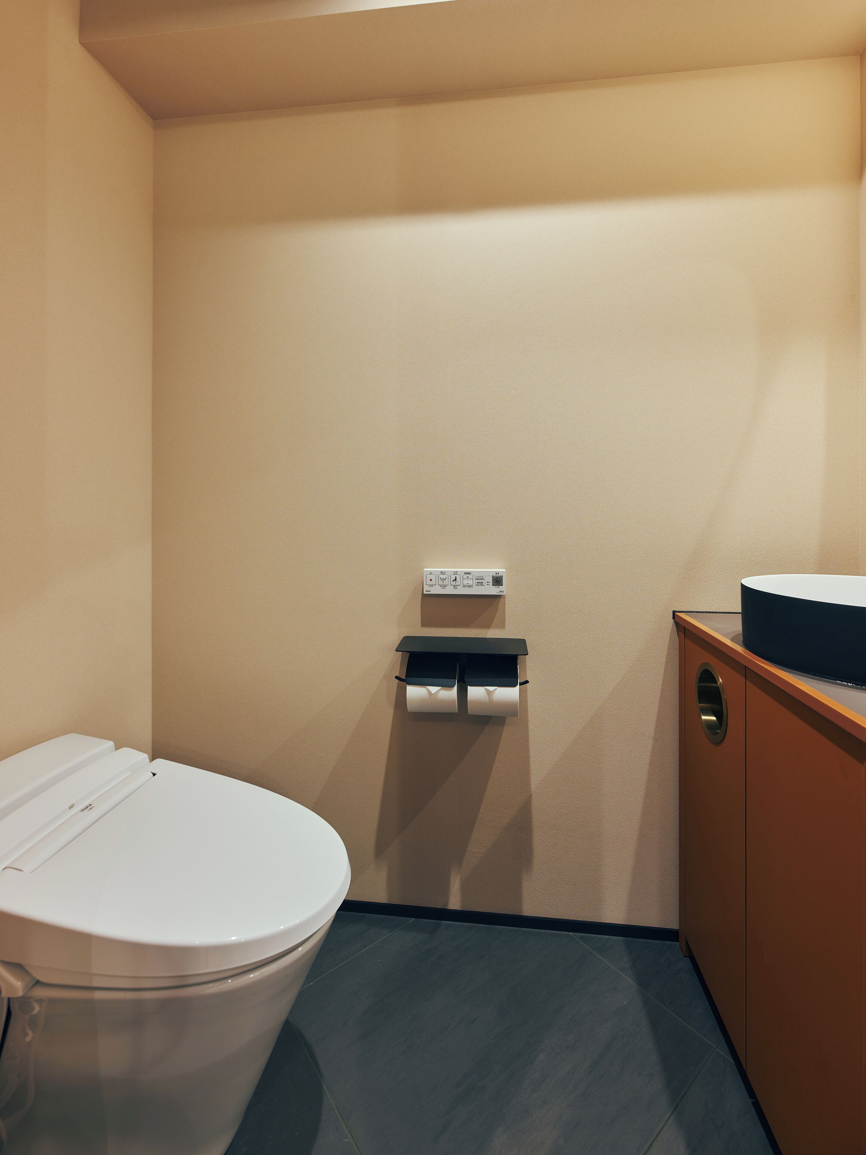 A small, compact bathroom with a toilet, a sink, and a wall-mounted paper towel dispenser.