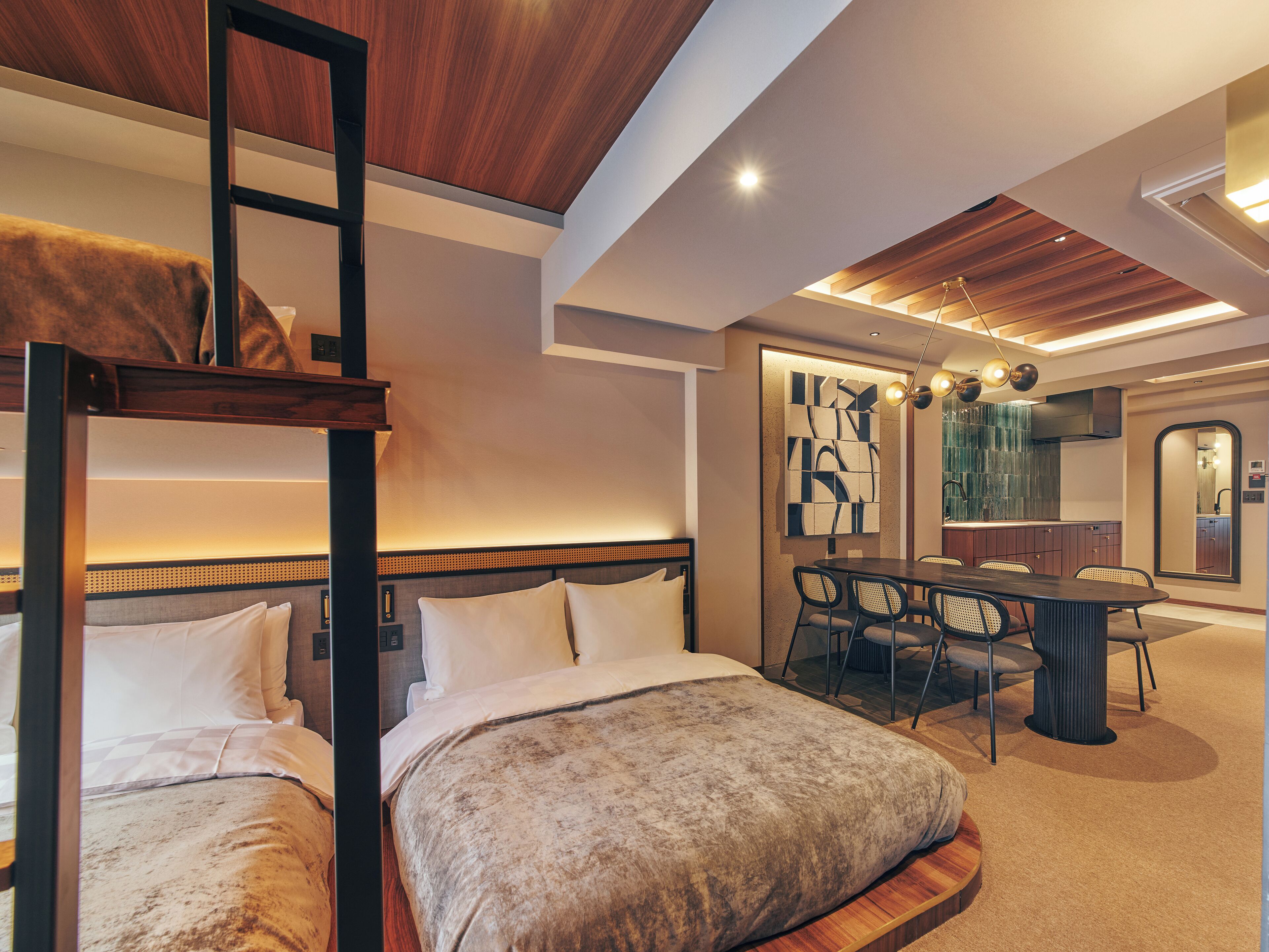 A hotel room with a bunk bed, a dining area with a table and chairs, and a kitchen area with a sink and mirror.