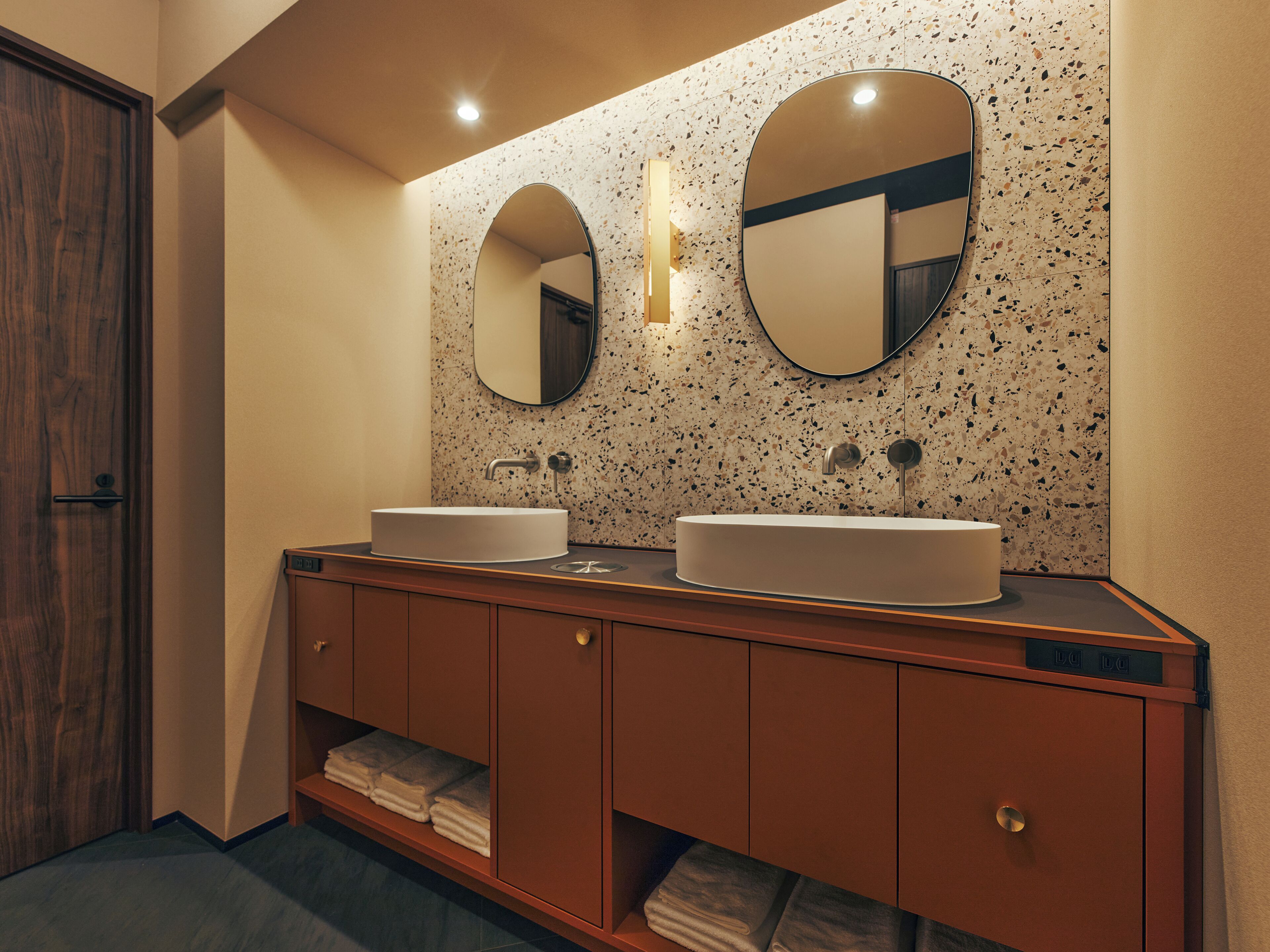A modern bathroom with two sinks, a wooden vanity, and a speckled backsplash.