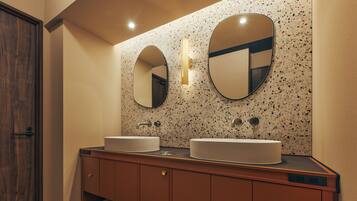 A modern bathroom with two sinks, a wooden vanity, and a speckled backsplash.