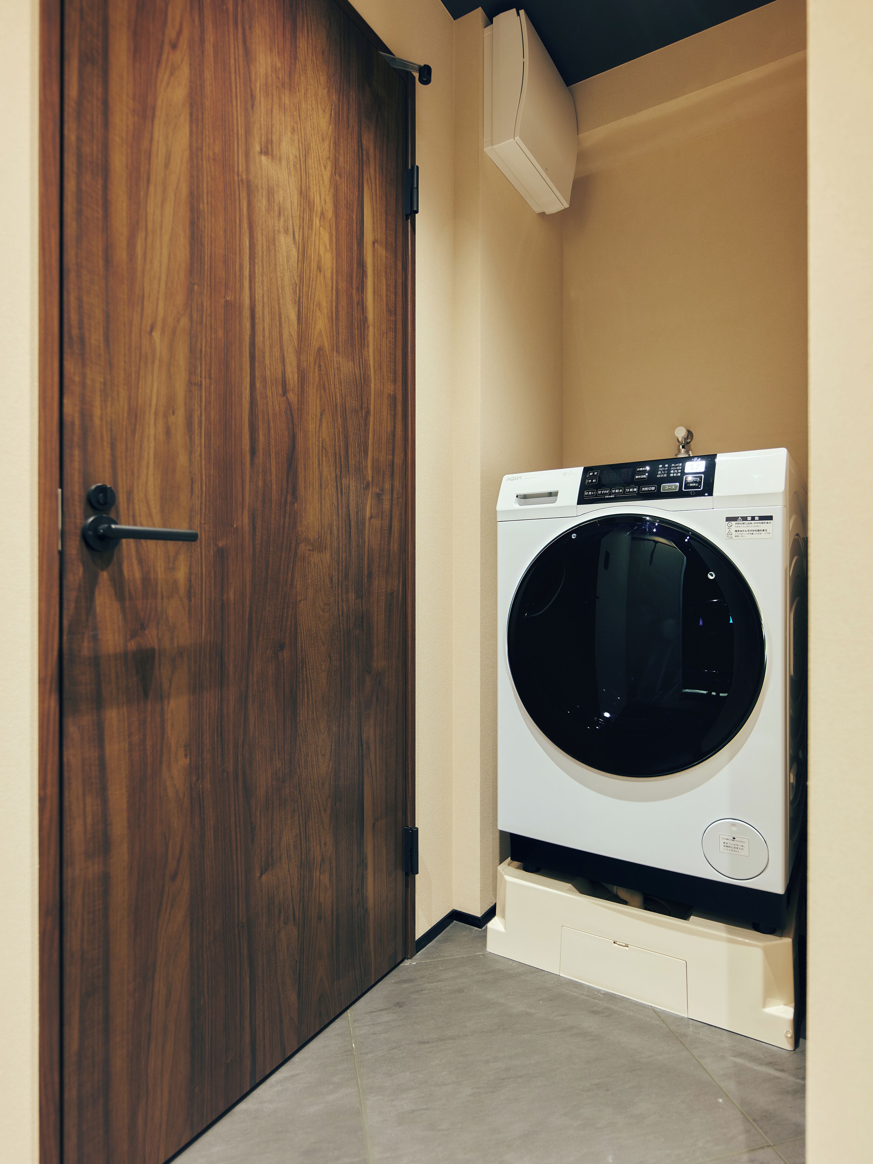 A laundry room with a wooden door and a front-loading washing machine.