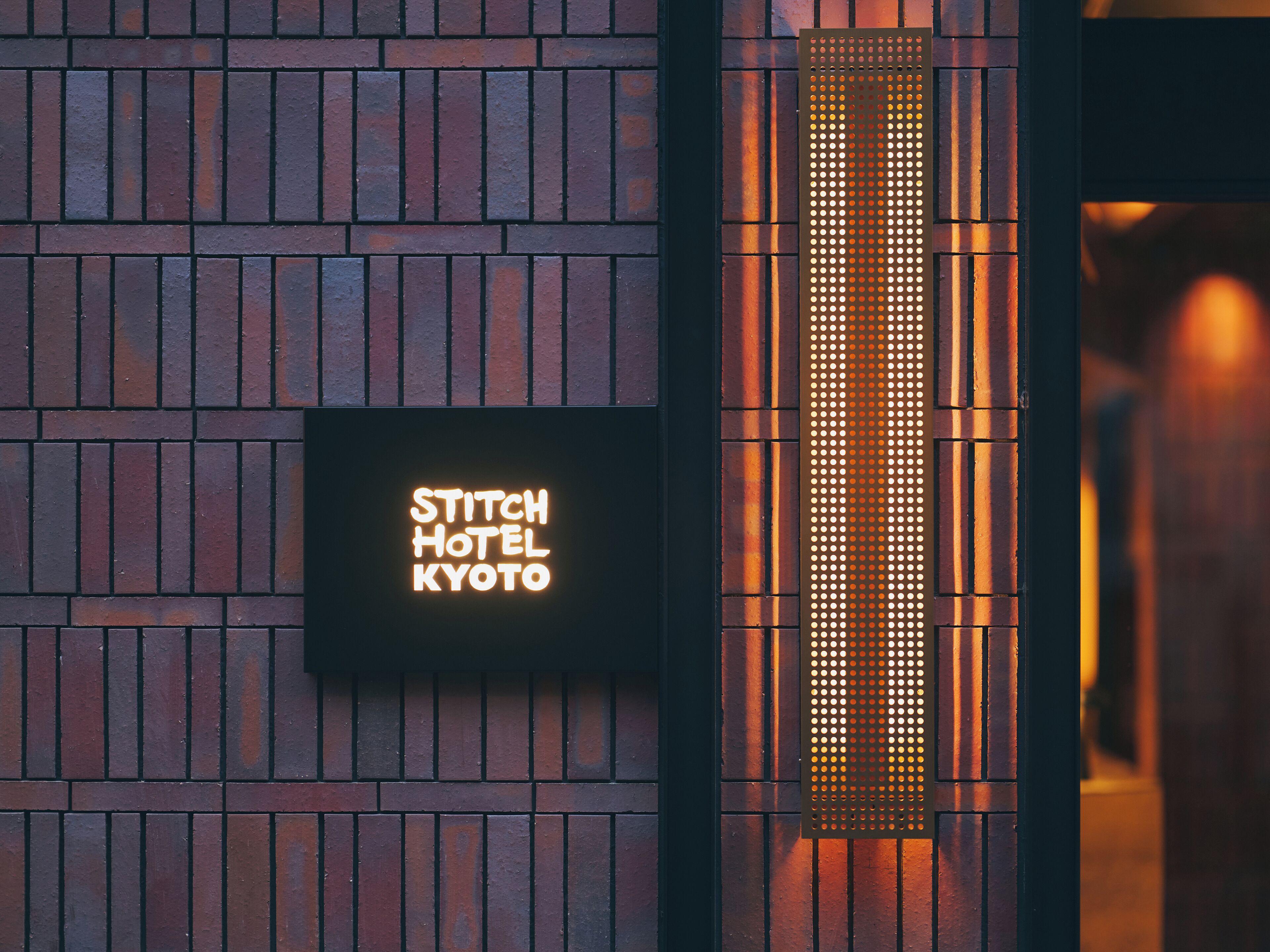 A brick wall with a neon sign reading "Stitch Hotel Kyoto".