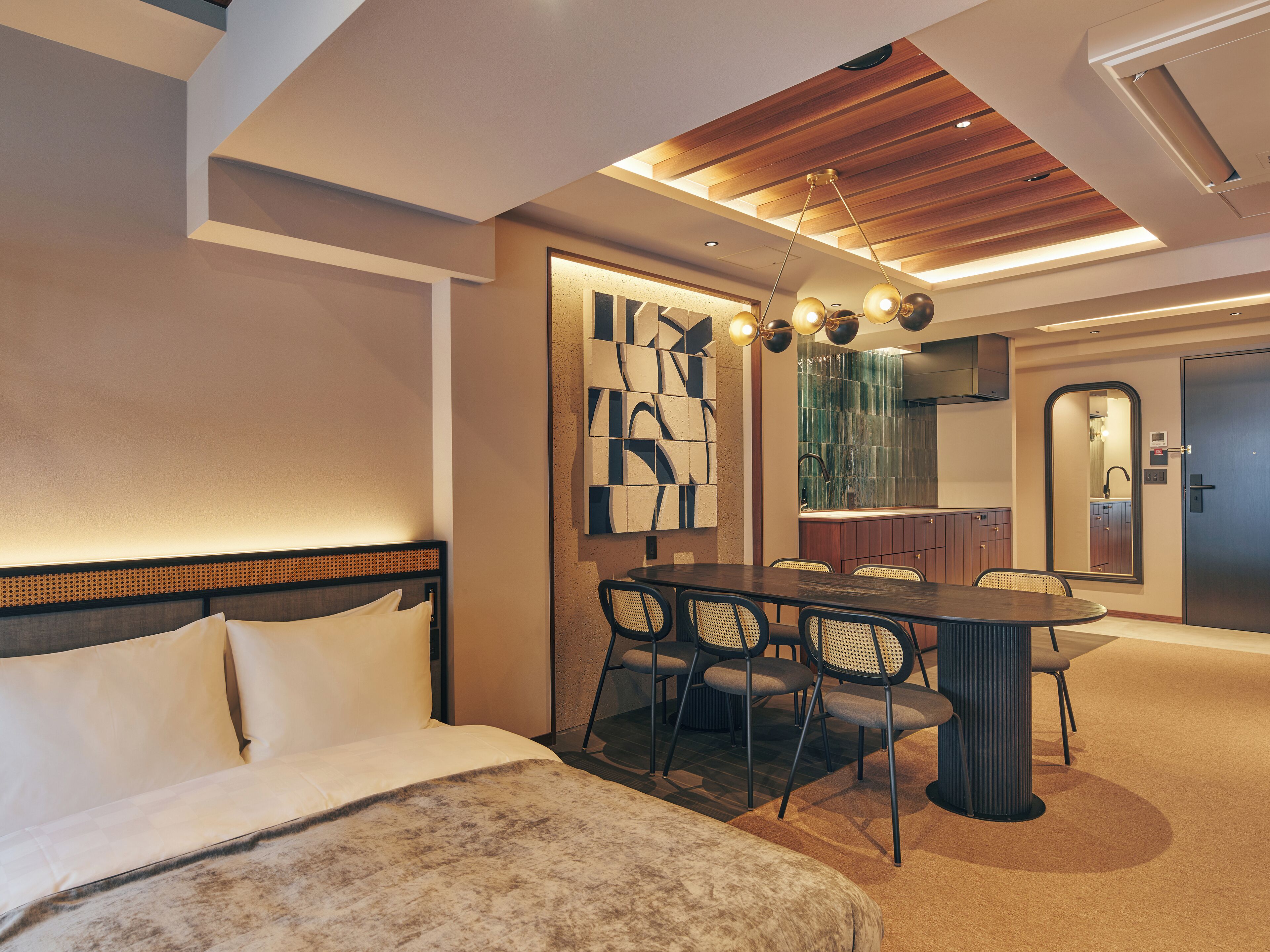 A modern hotel room with a bed, a dining area with chairs, a wooden ceiling, and a large mirror.