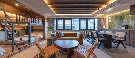 Un intérieur moderne avec une table ronde centrale, des sièges, un escalier et un coin cuisine.