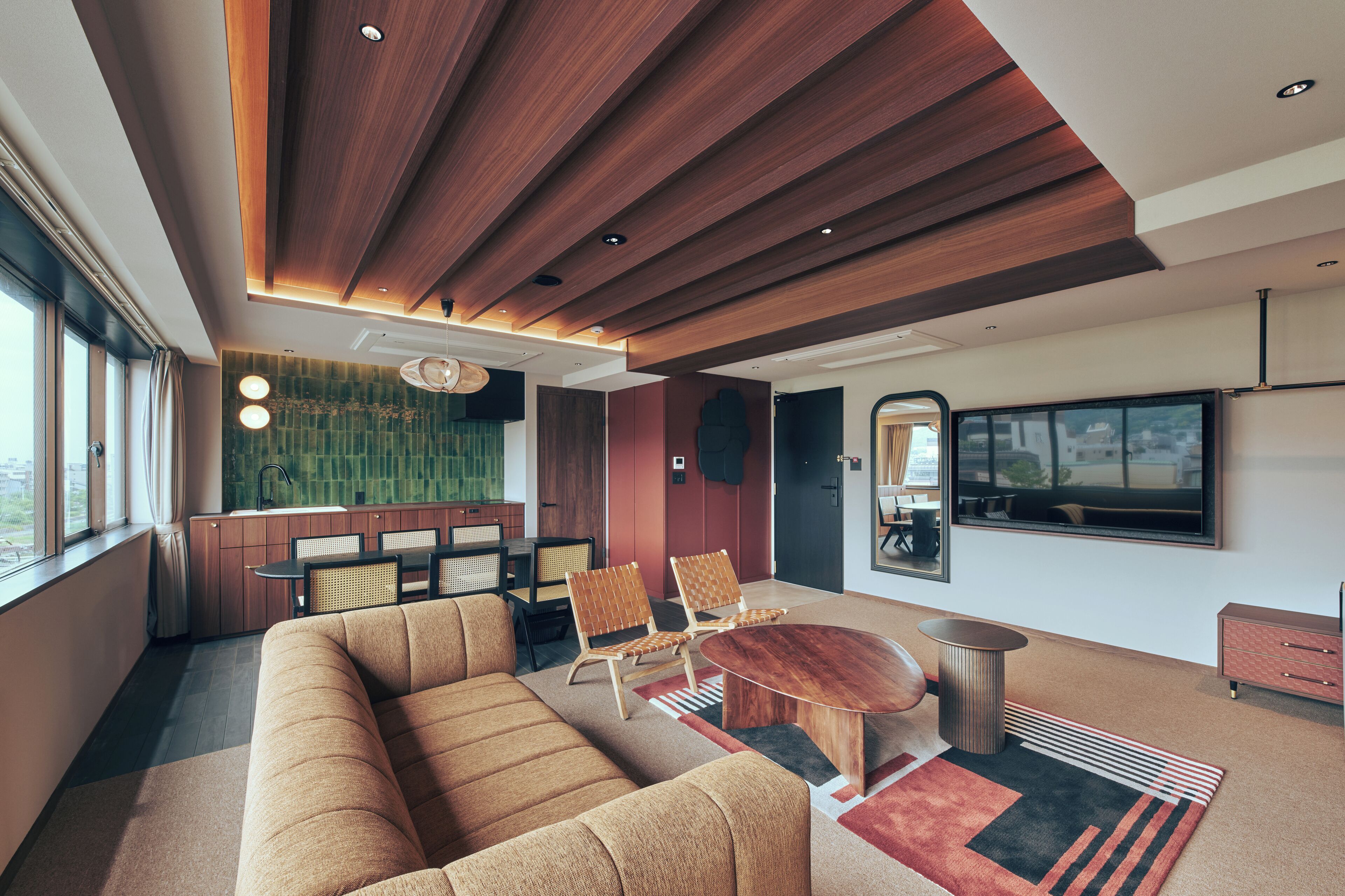A modern living room with a wooden ceiling, a large sofa, two armchairs, a round coffee table, and a television mounted on the wall.