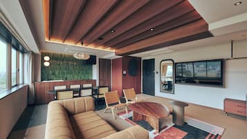 A modern living room with a wooden ceiling, a large sofa, two armchairs, a round coffee table, and a television mounted on the wall.
