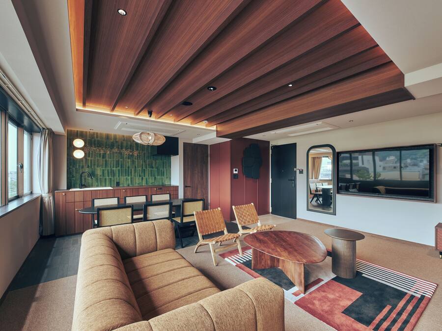 A modern living room with a wooden ceiling, a large sofa, two armchairs, a round coffee table, and a television mounted on the wall.
