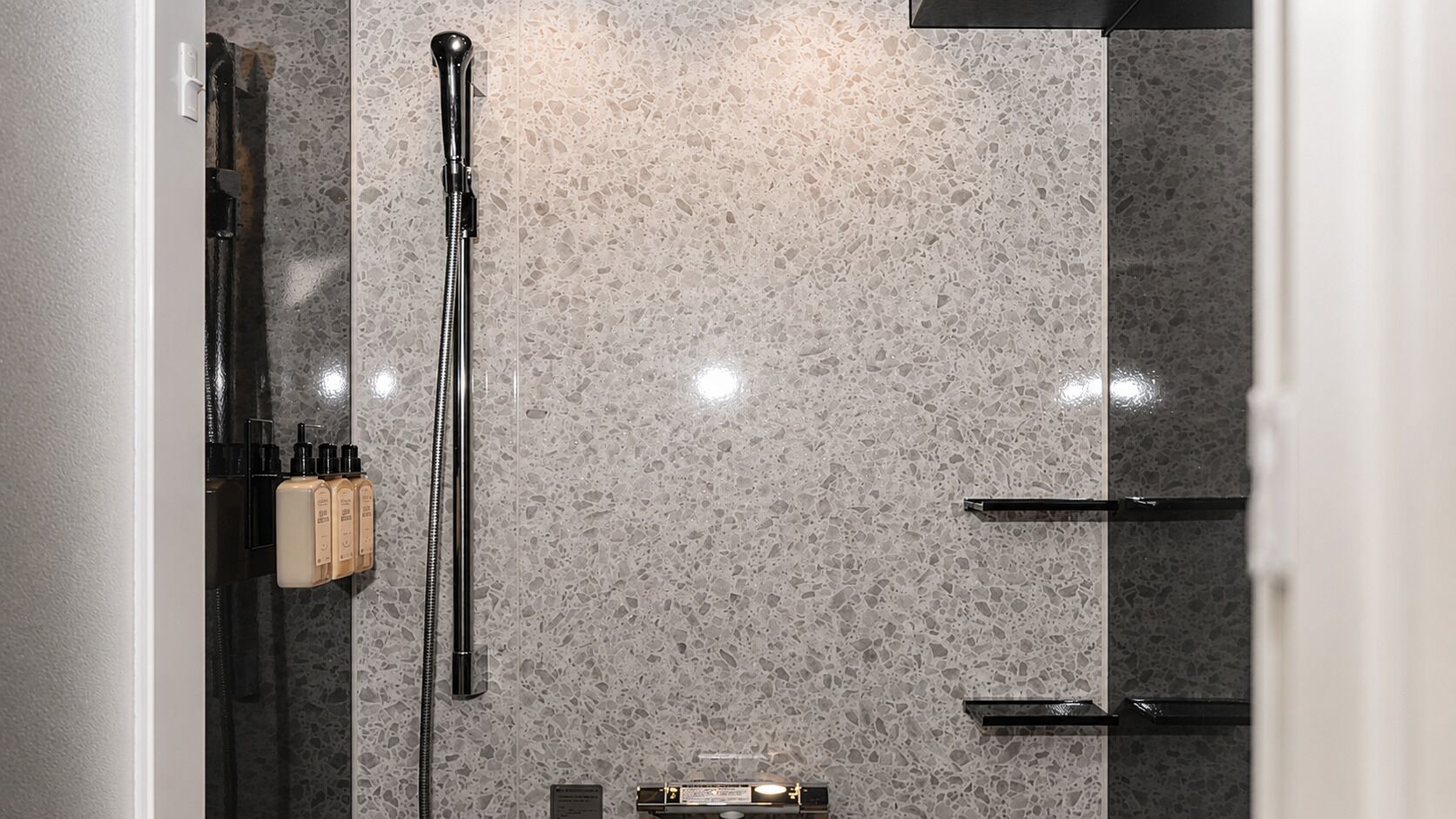 A bathroom with a shower, a towel rack, and a soap dispenser.