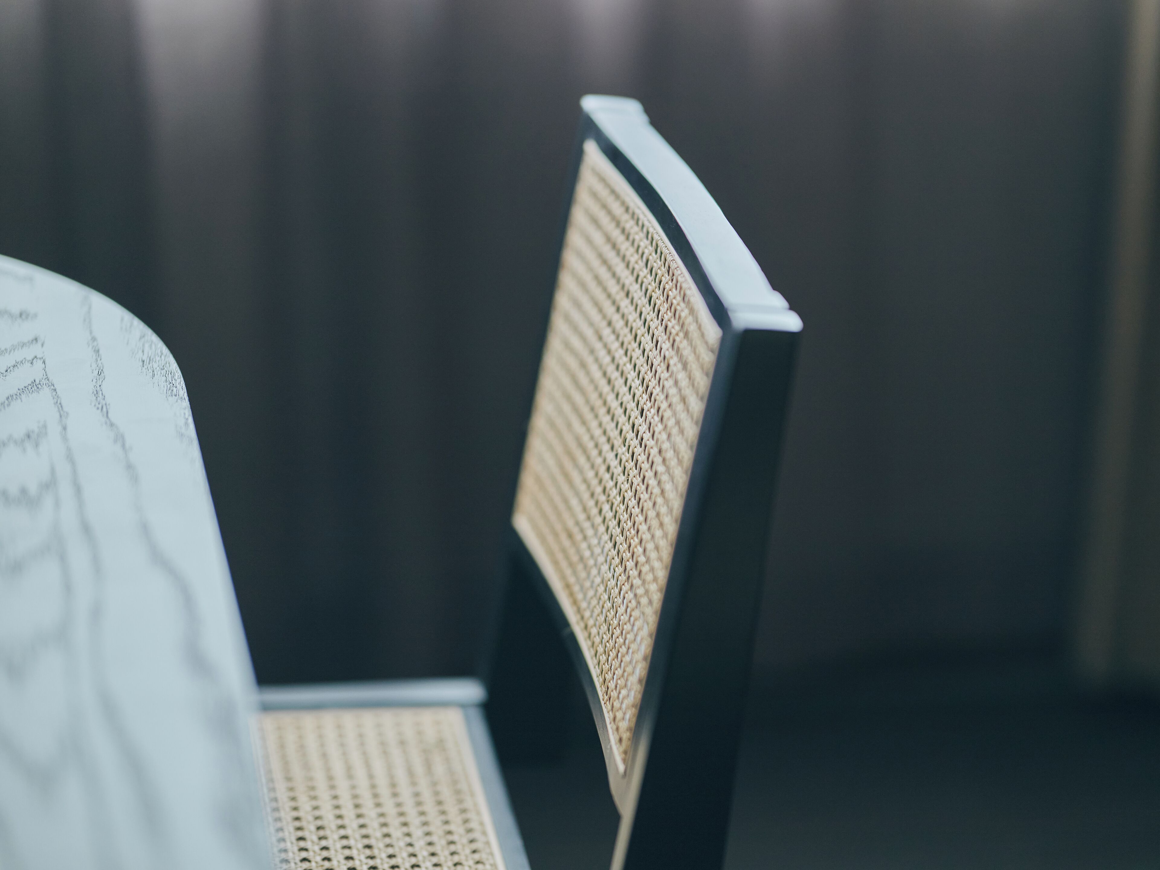 A chair with a woven backrest and a metal frame, positioned in a room with a dark background.