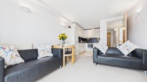 Ein modernes Wohnzimmer mit zwei schwarzen Ledersofas, einem Holzespeisetisch mit Blumenvase und einer Küche im Hintergrund.