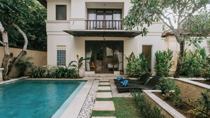 A poolside area with a clear pool, a covered seating area with lounge chairs, and a well-maintained garden with various plants. - Villa Anggrek Jimbaran (Jimbaran)