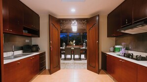 A kitchen with wooden cabinets, a dining table with chairs, and a view of the outdoors. - Villa Anggrek Jimbaran (Jimbaran)