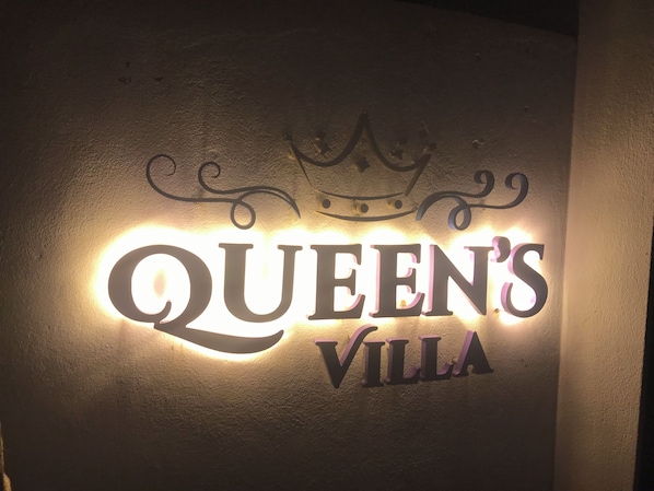 Un letrero con el texto 'Queen's Villa' y un símbolo de corona.