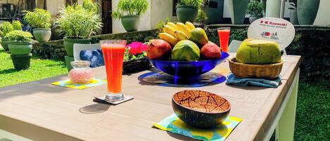 A table set outdoors with a fruit bowl, a glass of juice, and a bowl of food.