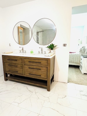 Une salle de bain avec un meuble-lavabo en bois, deux miroirs ronds, un évier et une plante en pot.