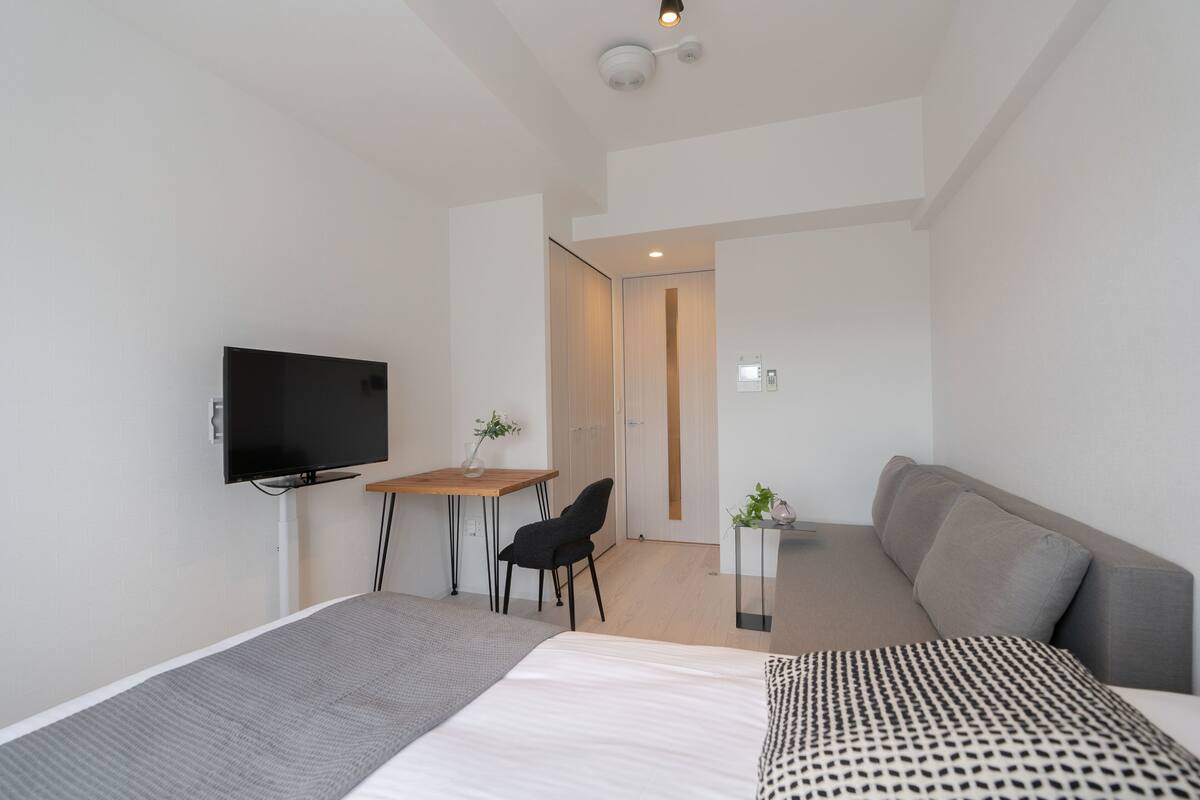 Une chambre d’hôtel moderne équipée d’un lit, d’un bureau, d’une chaise, d’une télévision et d’une petite table agrémentée d’une plante.