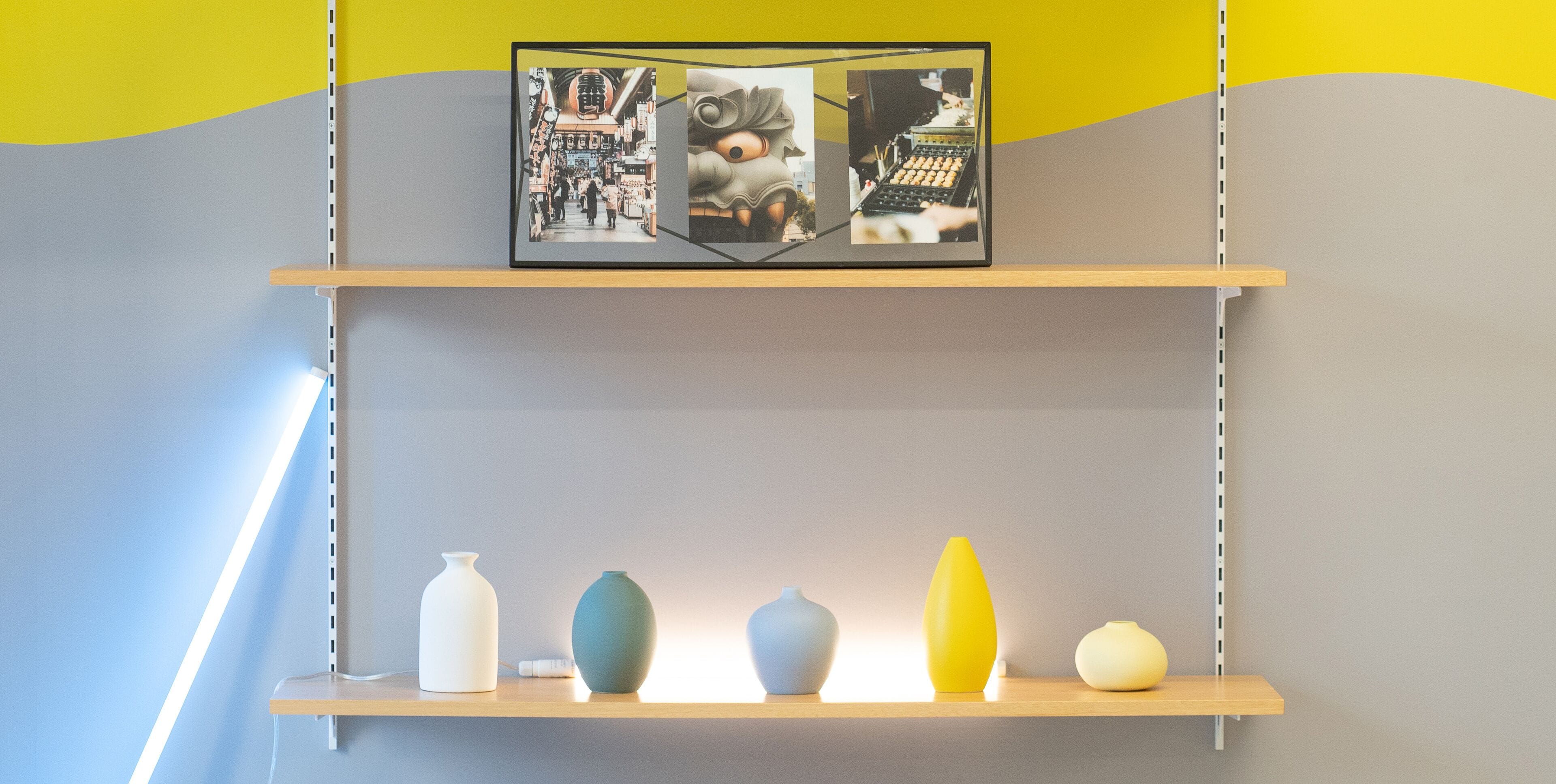 Uma prateleira com cinco vasos de cores variadas e uma moldura com uma fotografia em cima.