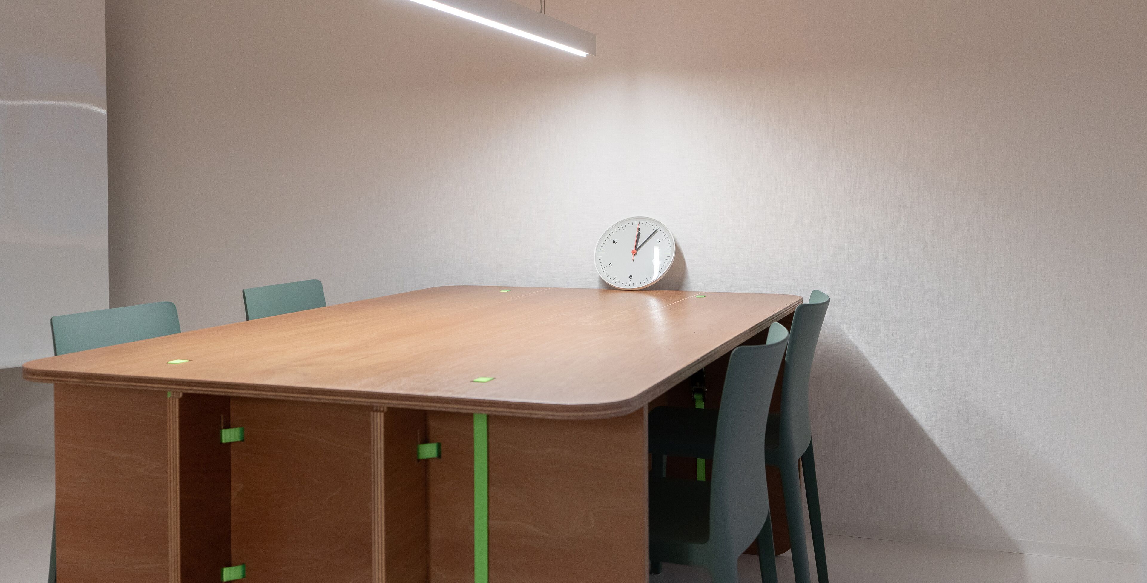 A conference room with a wooden table, four chairs, and a wall-mounted clock.