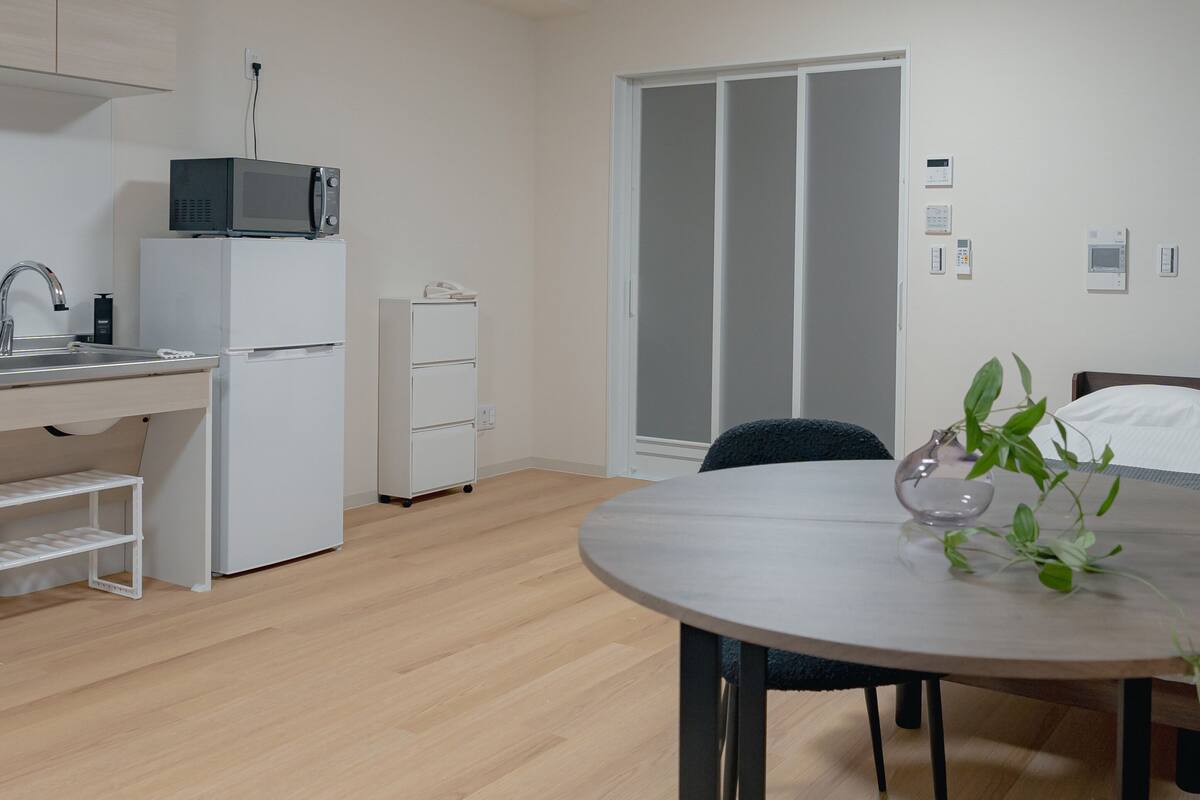 Une chambre d’hôtel compacte comprenant un coin cuisine, une table à manger ronde, un lit avec du linge de maison blanc et un placard avec porte coulissante.