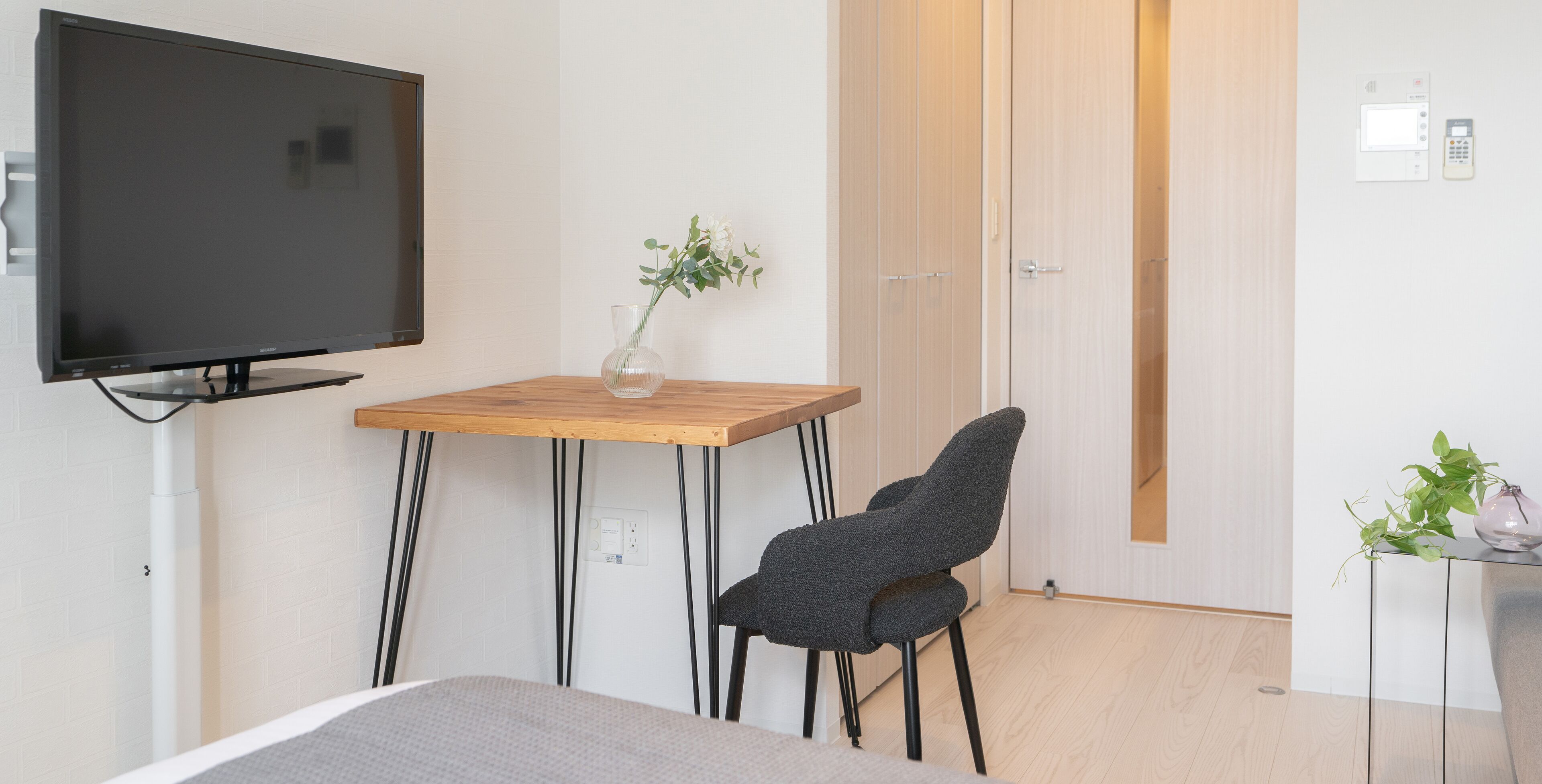 Una habitación de hotel moderna con una televisión de pantalla plana, una mesa de madera con un jarrón de flores, una silla gris y una cama.