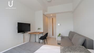 A modern hotel room with a bed, a desk, a chair, a sofa, and a television.