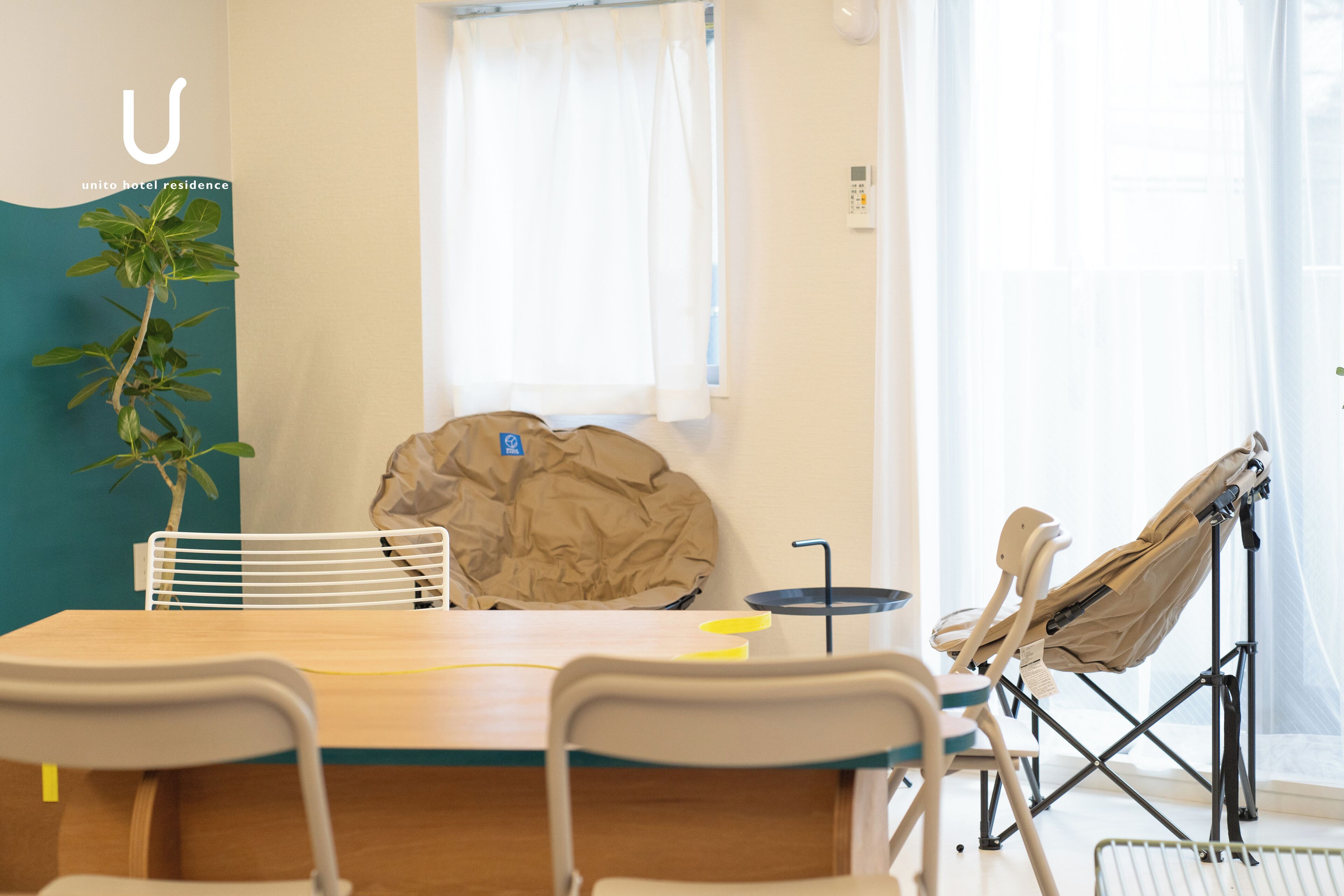 A room with a wooden table, white chairs, a beige bag, a baby stroller, and a potted plant.
