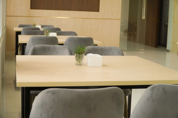 A modern dining area with a long table, grey chairs, and a small plant on the table. - Horison Resort Antawirya Jepara (Tahunan)
