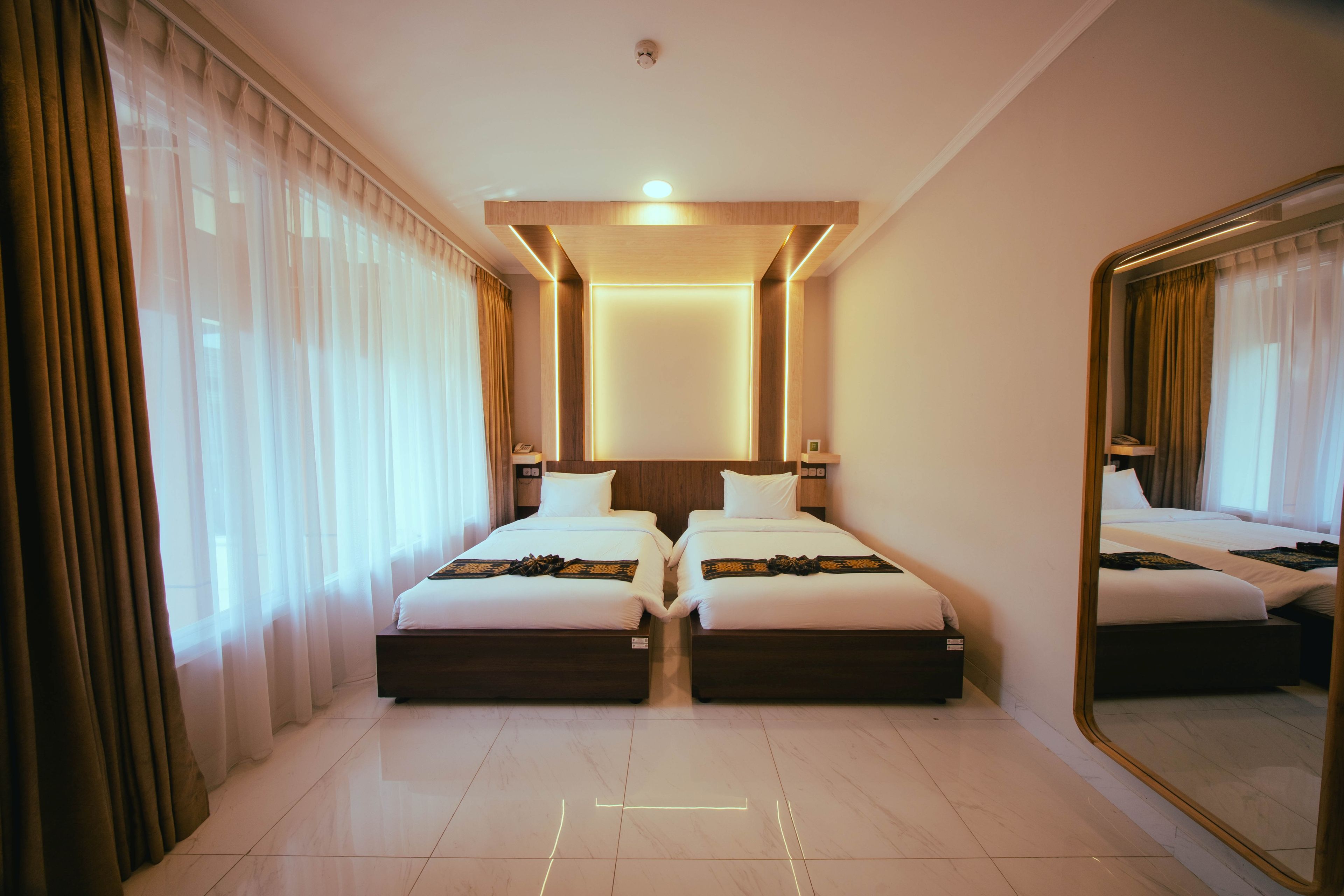 Une chambre d’hôtel avec deux lits, un grand miroir et un luminaire au plafond.