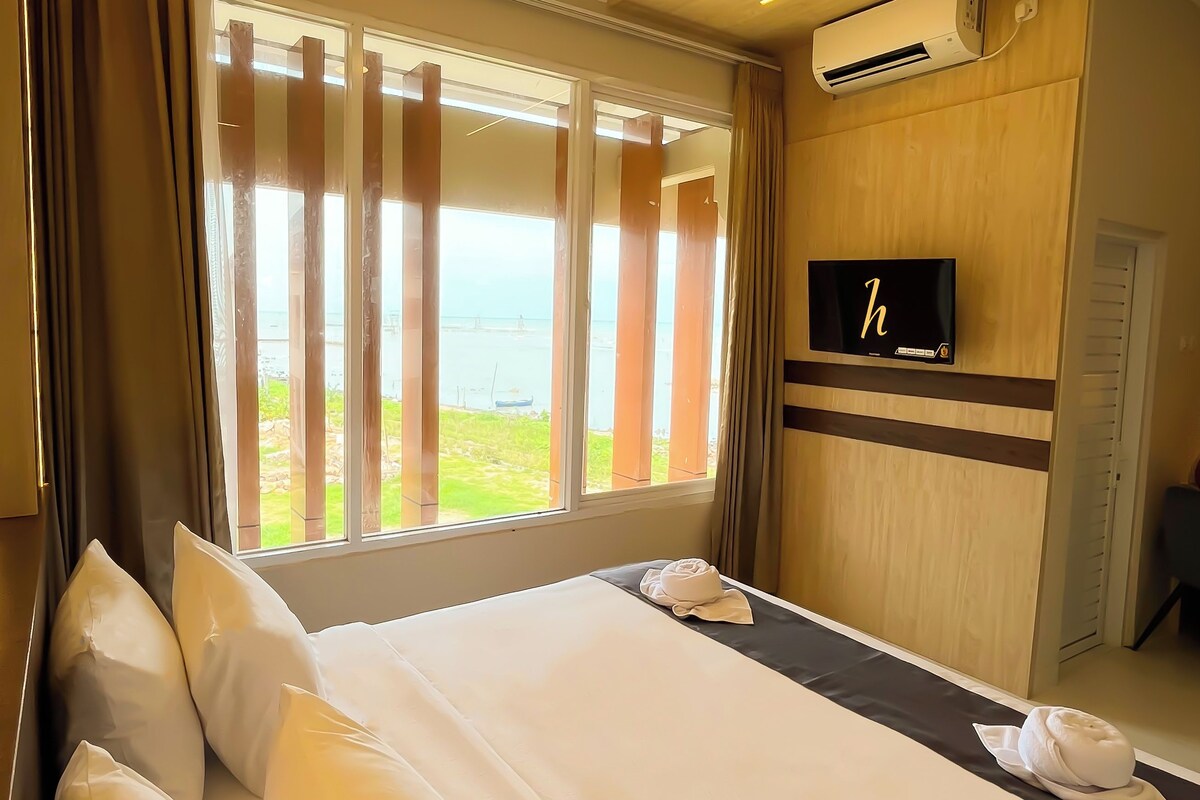 Een hotelkamer met een groot bed, een aan de muur bevestigde televisie en uitzicht op de zee.