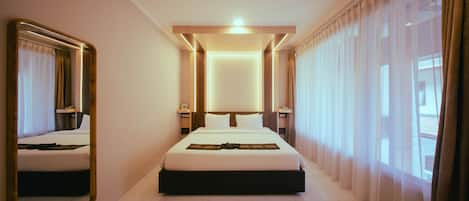 Una habitación de hotel con una cama grande, mesitas de noche, un espejo y vistas al exterior a través de cortinas translúcidas.