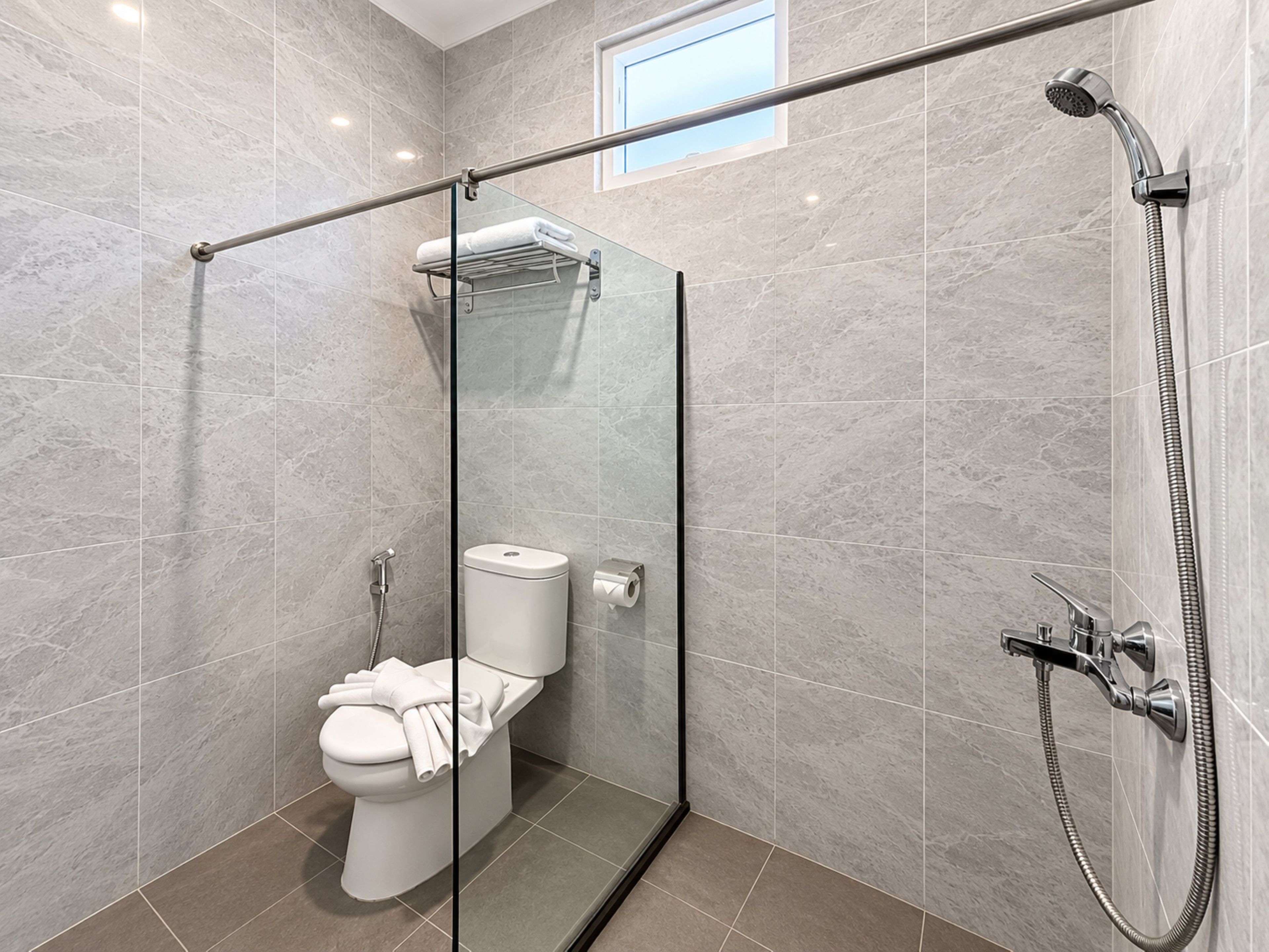 Une salle de bain moderne avec une douche à parois de verre, des toilettes et un porte-serviettes.
