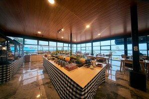 A breakfast bar with a checkered tablecloth, a coffee station, and a view of the sea through large windows. - Horison Resort Antawirya Jepara (Tahunan)