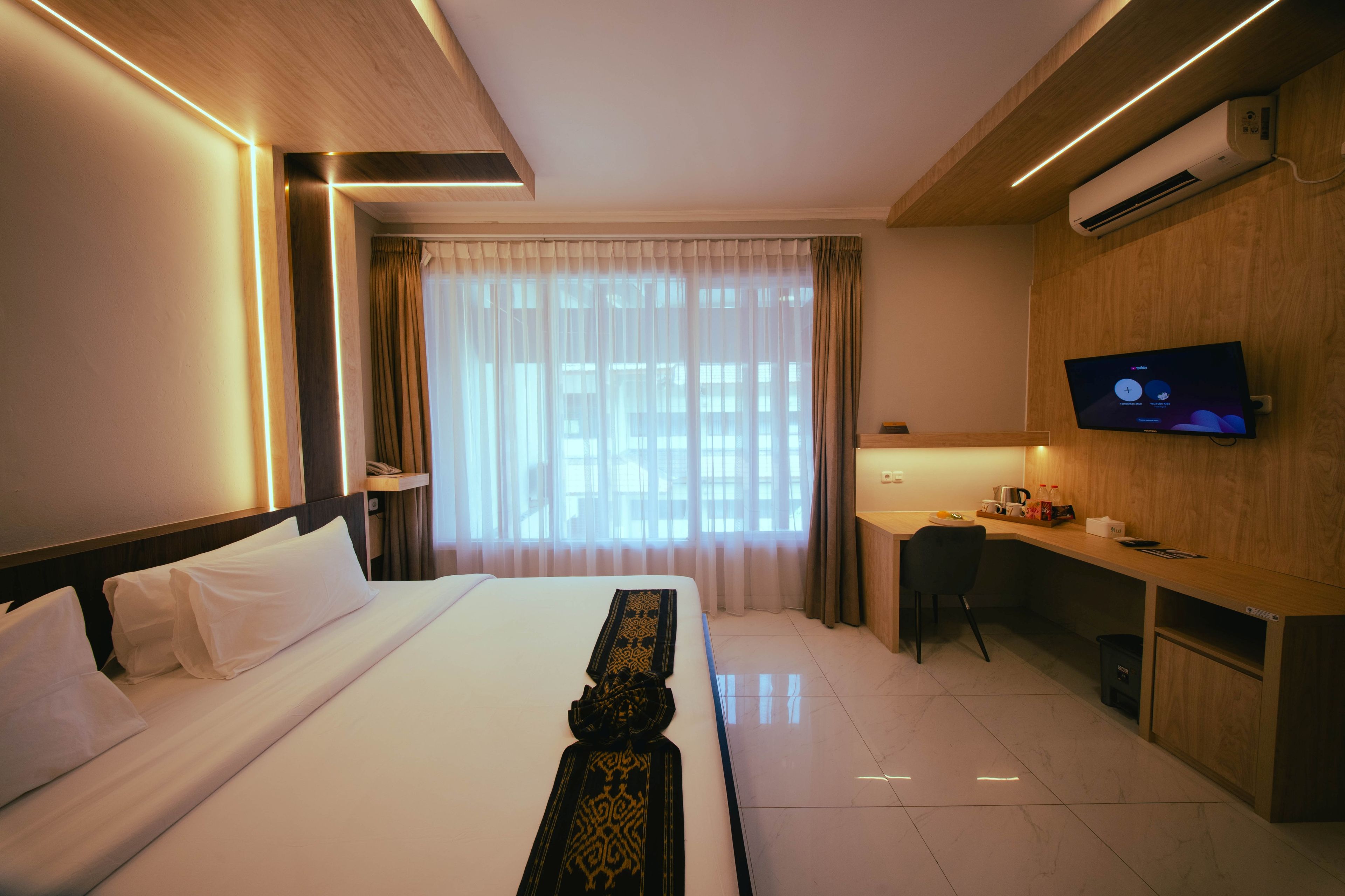 A hotel room with a bed, a desk, a television, and an air conditioning unit.