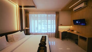 A hotel room with a bed, a desk, a television, and an air conditioning unit.