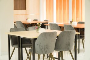 Une salle de conférence avec plusieurs tables et chaises, un vase rempli de fleurs et une fenêtre avec des rideaux.